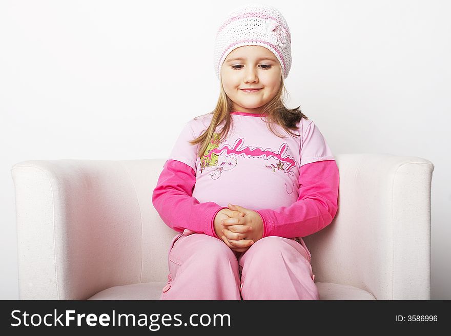 Nice young girl in pink on light background sitting on white chair with teddy bear