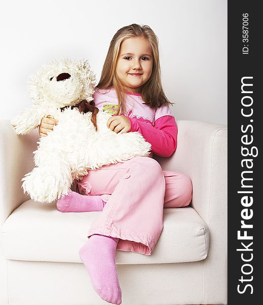 Nice young girl in pink on light background sitting on white chair with teddy bear