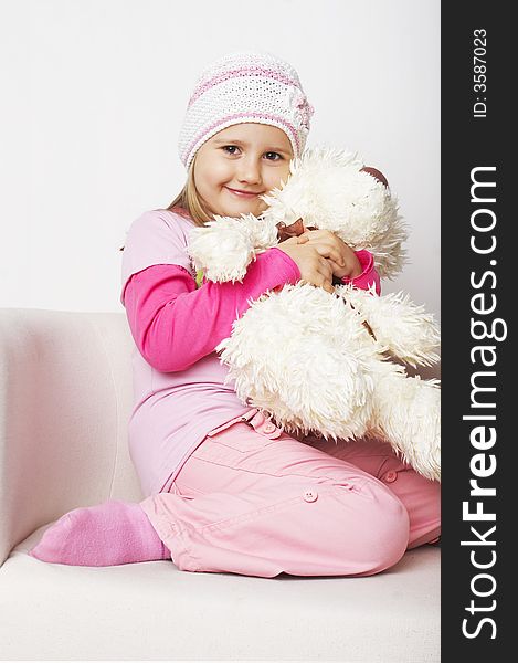 Nice young girl in pink on light background sitting on white chair with teddy bear