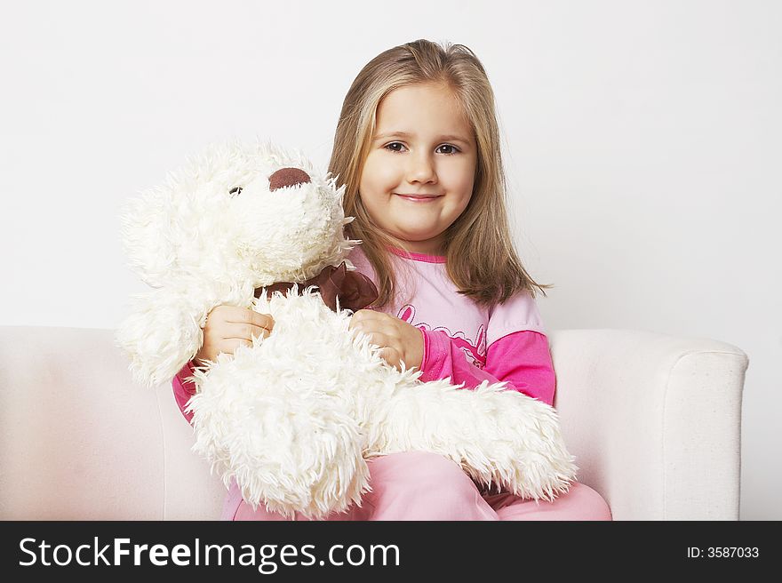 Nice young girl in pink on light background sitting on white chair with teddy bear