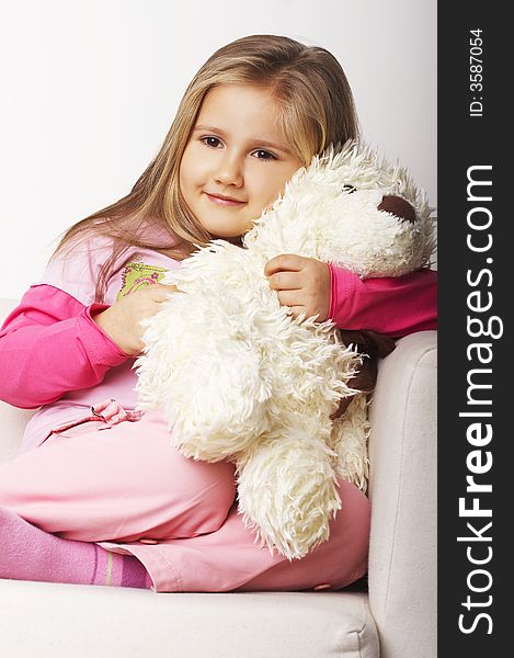 Nice young girl in pink on light background sitting on white chair with teddy bear