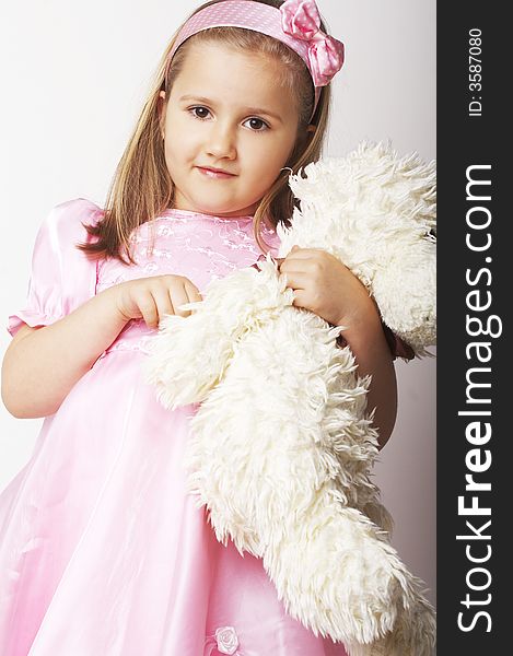 Nice young girl in pink on light background standing on white chair with teddy bear