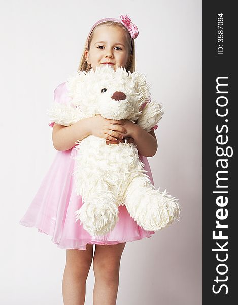 Nice young girl in pink on light background standing on white chair with teddy bear