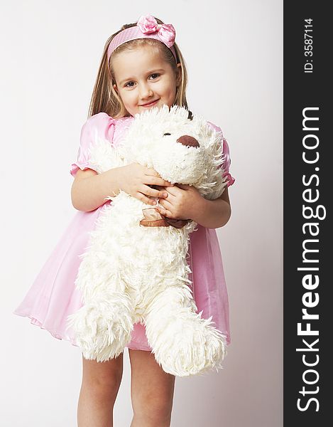 Nice young girl in pink on light background standing on white chair with teddy bear