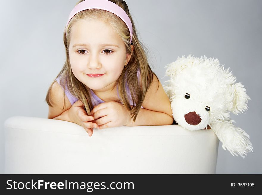 Nice young girl in pink on light background sitting on white chair with teddy bear