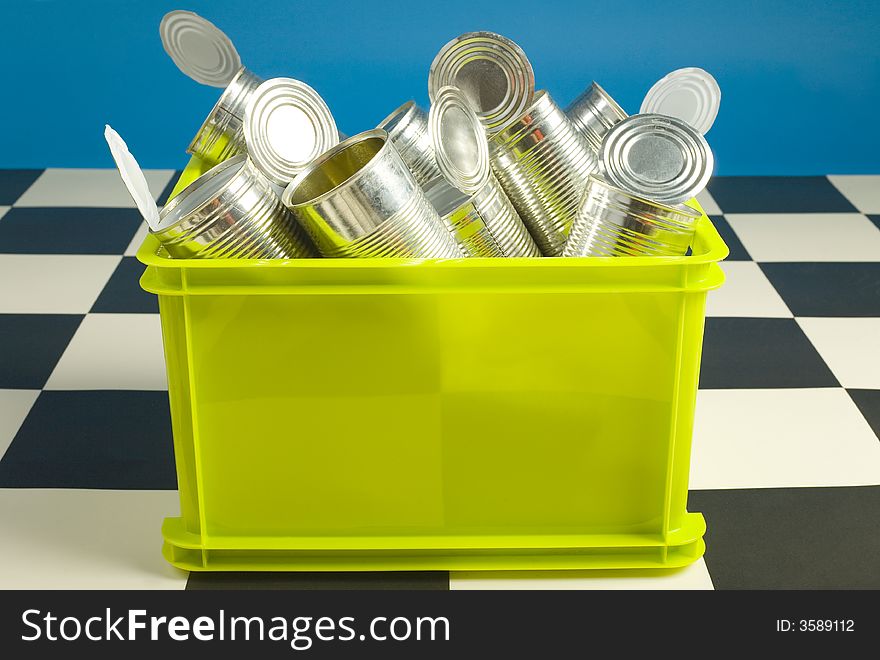 Green bin full up with tins standing on floor. Front iew