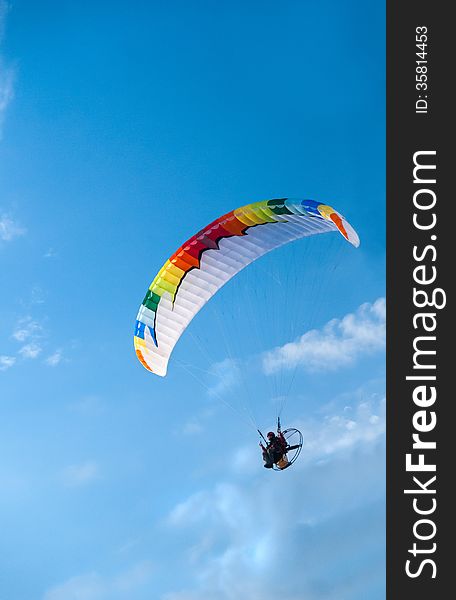 Vertical photo of motor powered paragliding, against blue sky.