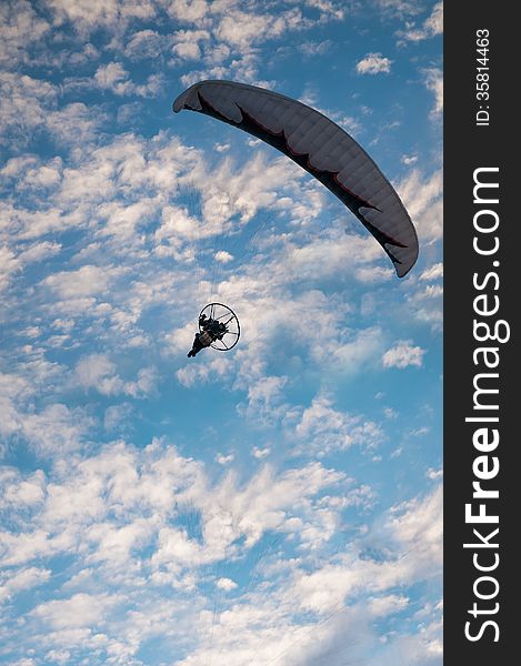 Vertical photo of motor powered paragliding, against blue sky.