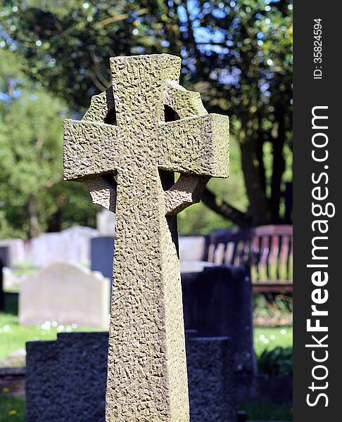 Celtic cross in cemetery with trees in background.