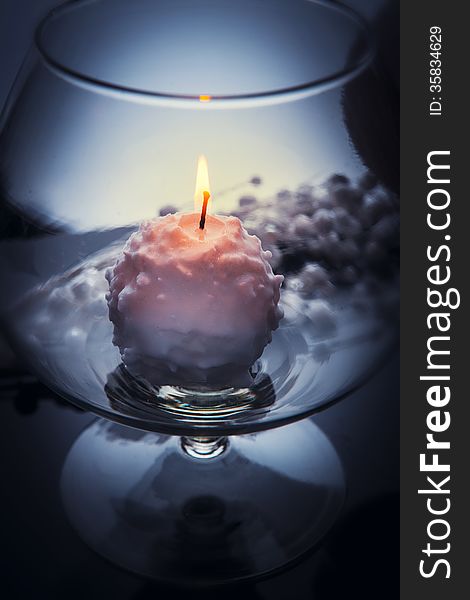 Small white candle burning and melting like a snowball inside big glass goblet. Over grey tint, blurred background. Small white candle burning and melting like a snowball inside big glass goblet. Over grey tint, blurred background.