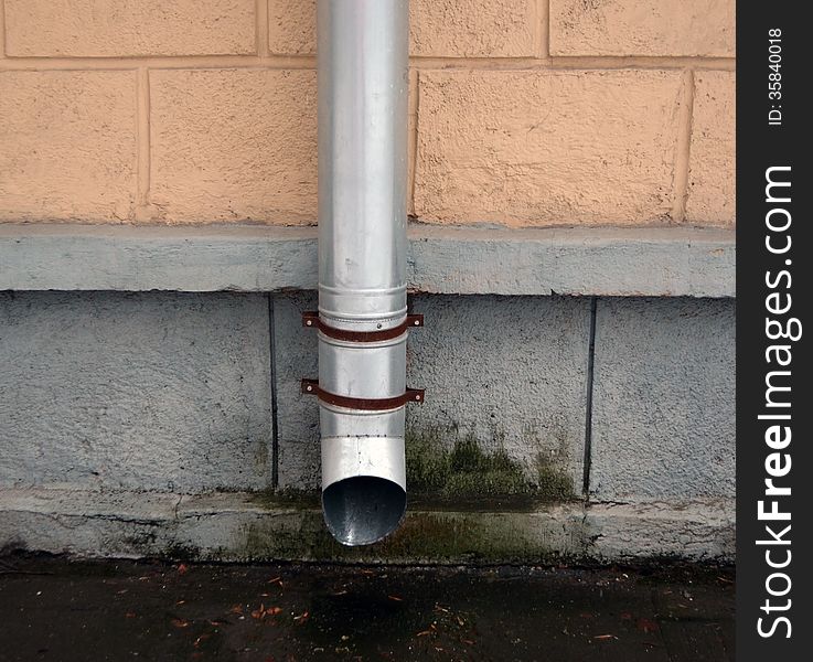 Drainpipe against a wall of a town house in cloudy weather.