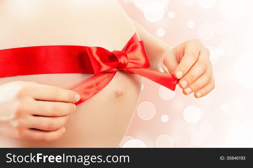 Belly of pregnant woman with red ribbon and bow