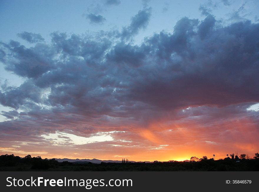 Dramatic blue grey clouds and orange pink sunset over South African farm. Dramatic blue grey clouds and orange pink sunset over South African farm.