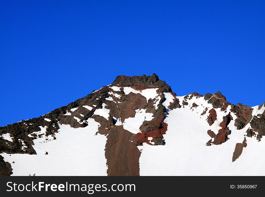 The jagged peak of Broken Top Mountain covered in snow with blue sky background rising above the Three Sisters Wilderness in central Oregon.