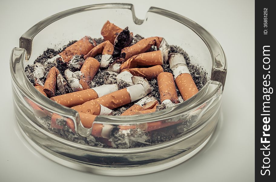 Cigarette butts in a glass ashtray vintage retro style background.