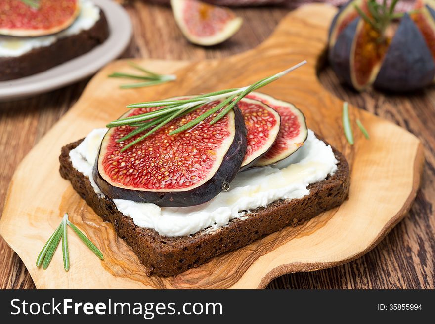 Bread with goat cheese, figs, honey and rosemary on a wooden board, close-up. Bread with goat cheese, figs, honey and rosemary on a wooden board, close-up