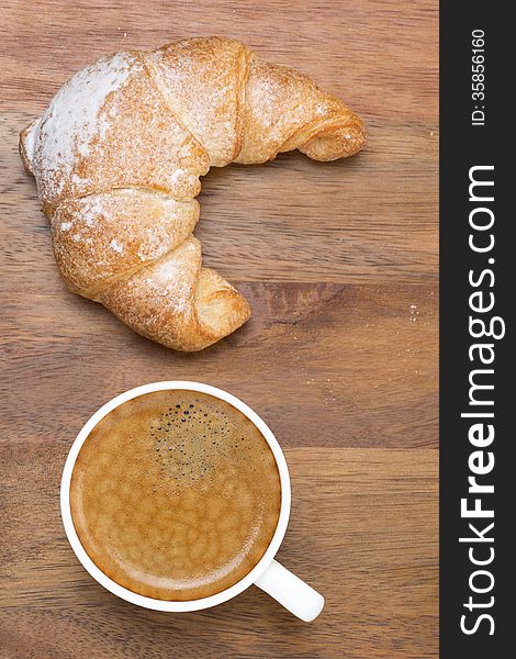 Croissant and a cup of black coffee on a wooden background, top view, vertical