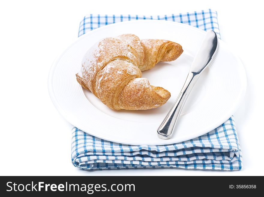 Fresh croissant and a knife on a plate isolated