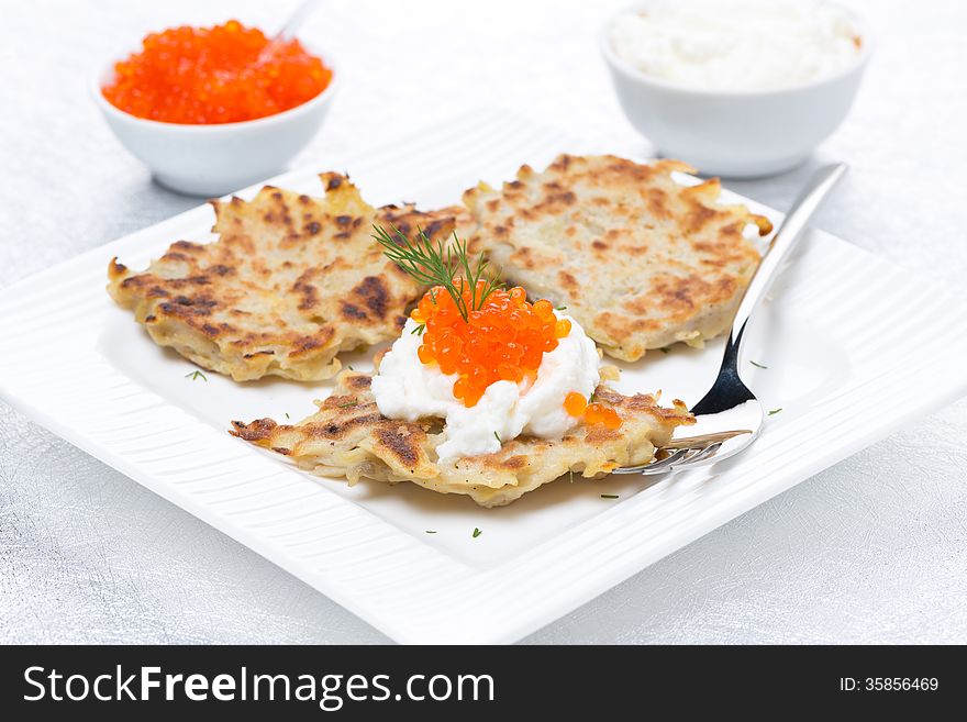 Potato pancakes with red caviar and sour cream on the plate, close-up