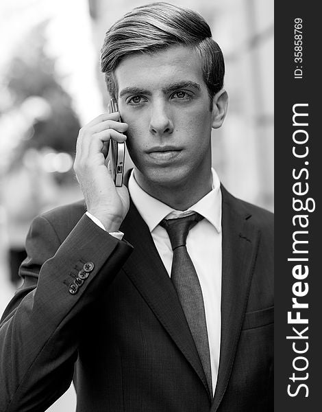 Portrait of an attractive young businessman on the phone in urban background, wearing blue suit and tie. Blonde hair