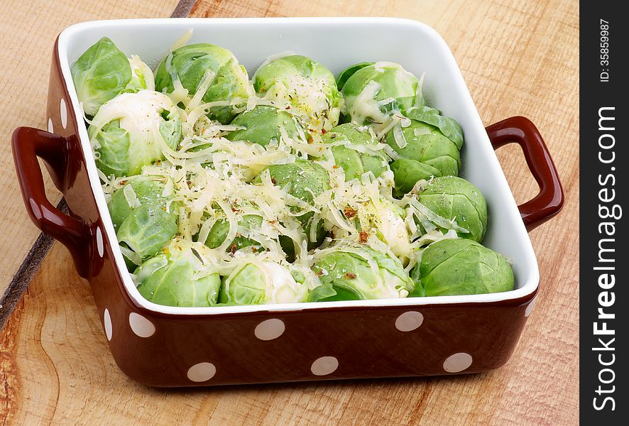 Delicious Brussels Sprouts Casserole with Grated Cheese and Spices in Brown Polka Dot Bowl closeup on Wooden background