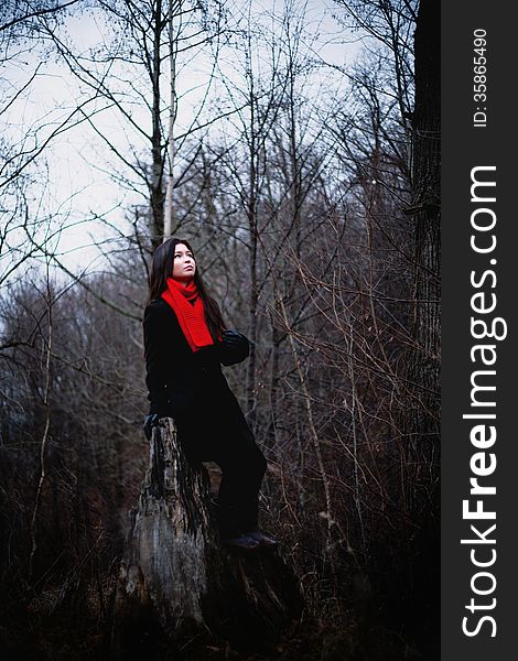 Woman in black coat and red scarf sitting in cold dark forest