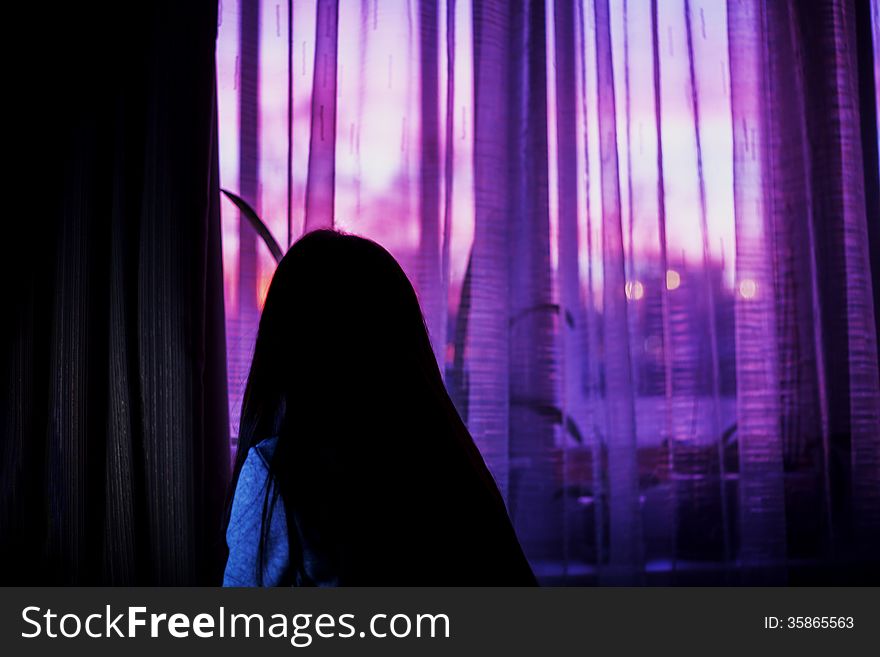Woman in dark room on sunset window background