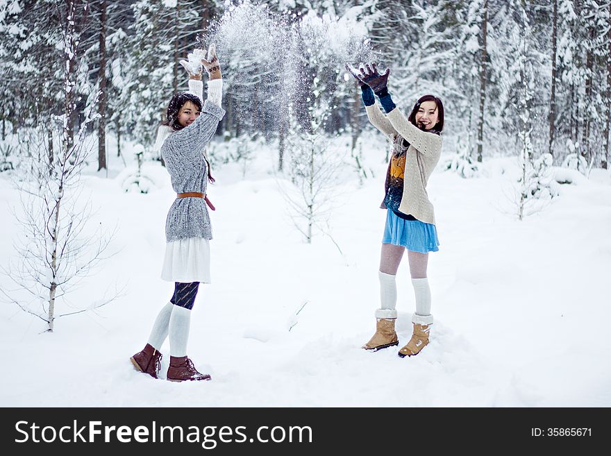 Fashion women in warm sweaters playing with snow on white forest background