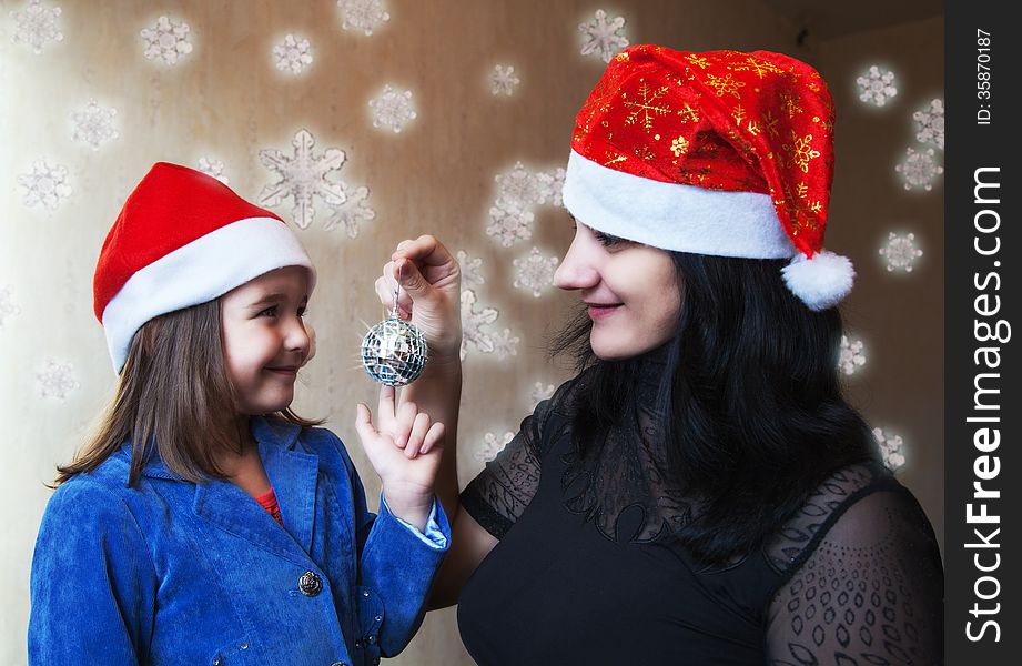 Mother and daughter in Christmas caps holding mirror ball