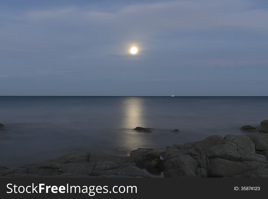 Reflections of the moon in the sea of ​​Calaliberotto, Sardinia! One of the most beautiful beach in Sardinia. Artistic view of the Moon path over the night sea with rocks and shore in the foreground. Shot with long exposure after the sunset.