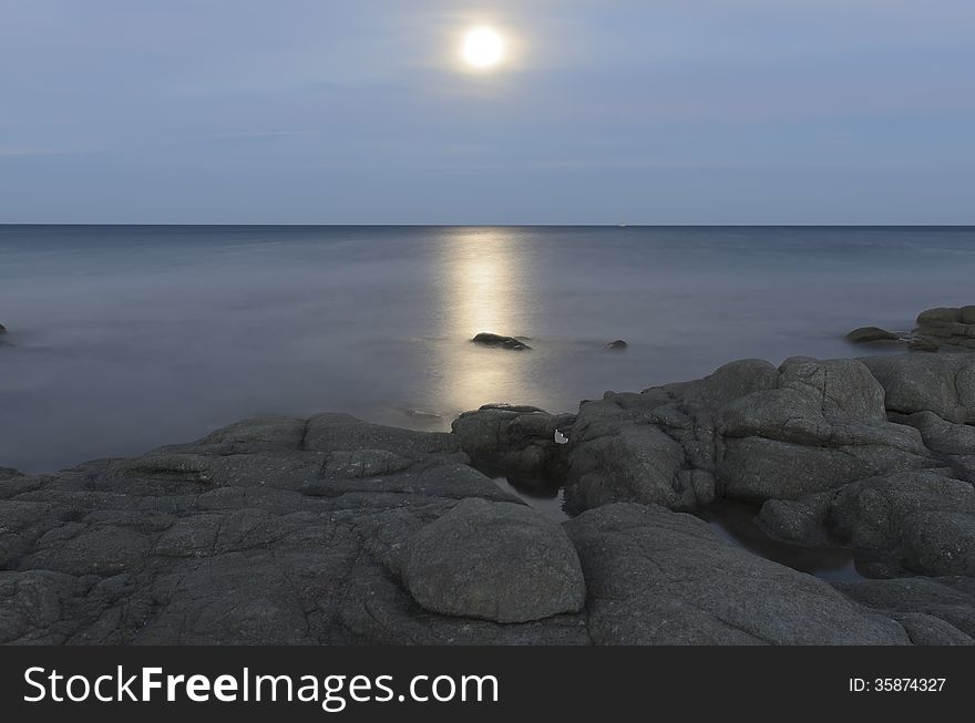 Reflections of the moon in the sea of â€‹â€‹Calaliberotto, Sardinia! One of the most beautiful beach in Sardinia. Artistic view of the Moon path over the night sea with rocks and shore in the foreground. Shot with long exposure after the sunset.