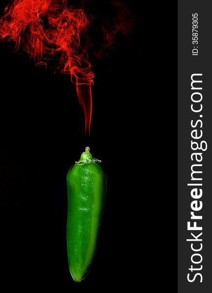 Green Chili pepper with red smoke rising from stim on black background. Green Chili pepper with red smoke rising from stim on black background