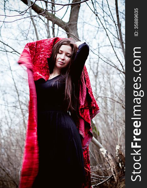 Woman in black dress with red fabric in cold dark forest