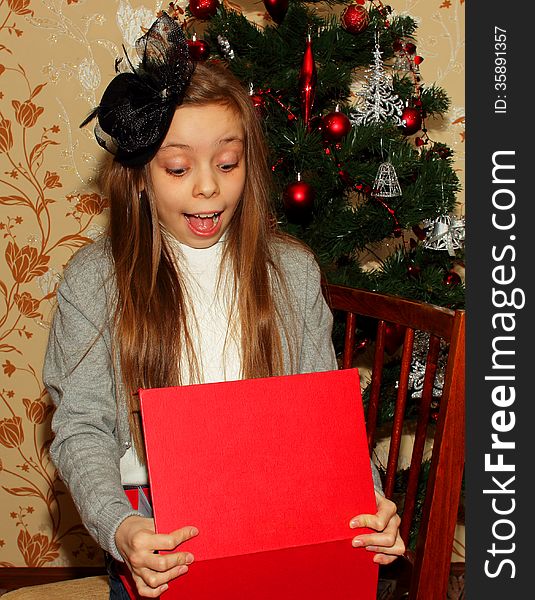 Girl in hat sitting near the Christmas tree and opened his gift greatly surprised. Girl in hat sitting near the Christmas tree and opened his gift greatly surprised