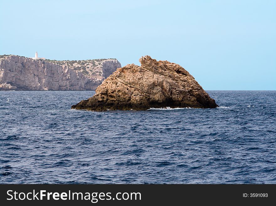 Large rock in the water near the west coast of Ibiza, Conejera island with its lighthouse Cabo Blanco in the background. Large rock in the water near the west coast of Ibiza, Conejera island with its lighthouse Cabo Blanco in the background