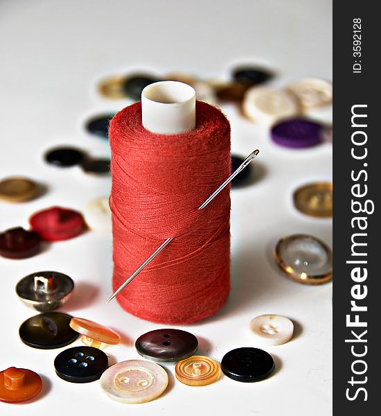 Reel of red thread with needle and scattered buttons. Reel of red thread with needle and scattered buttons