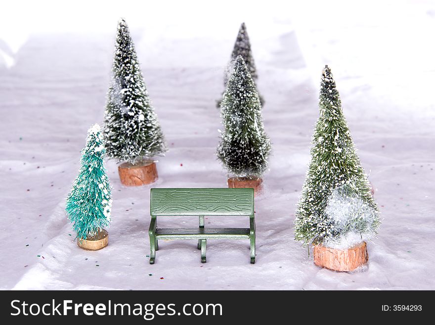 Miniature park bench with snow covered Christmas trees on snow cotton background. Miniature park bench with snow covered Christmas trees on snow cotton background.