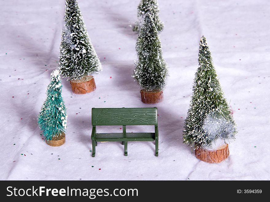 Miniature park bench with snow covered Christmas trees on snow cotton background. Soft shadowing added for realism. Miniature park bench with snow covered Christmas trees on snow cotton background. Soft shadowing added for realism.