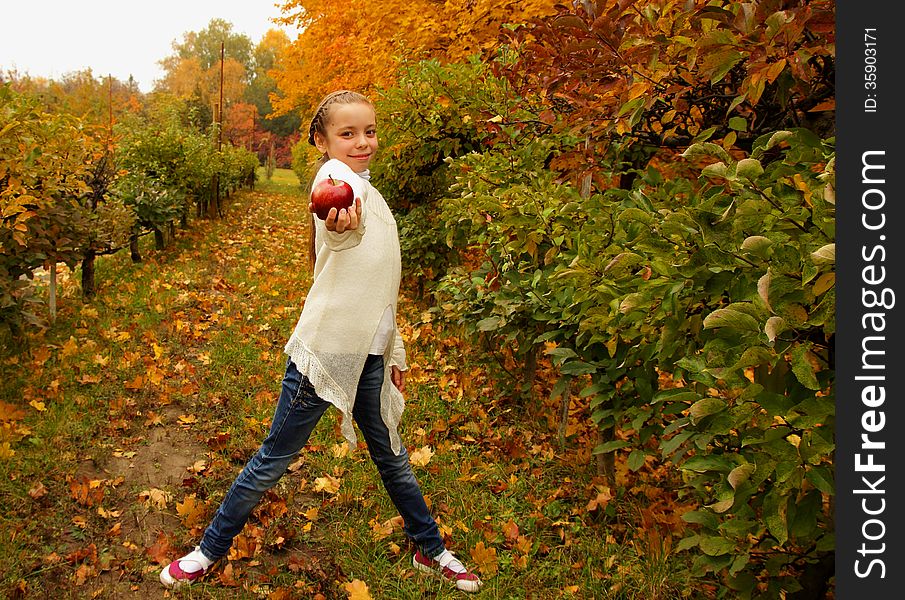 Pretty girl holding a red apple in hand on background of the autumn garden. Pretty girl holding a red apple in hand on background of the autumn garden