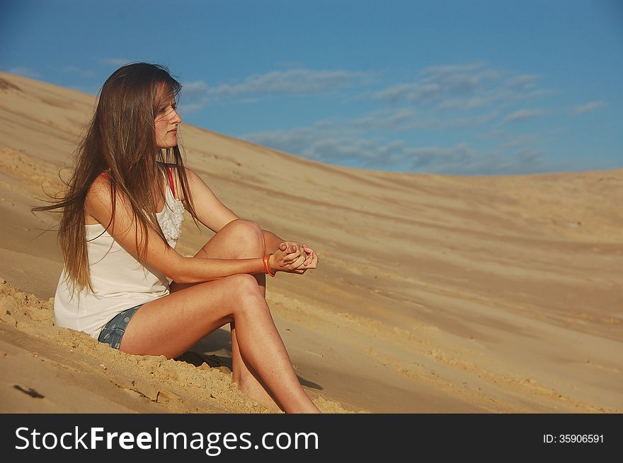 A pretty young teenager with long hair sits on a beach looking thoughtful. A pretty young teenager with long hair sits on a beach looking thoughtful.