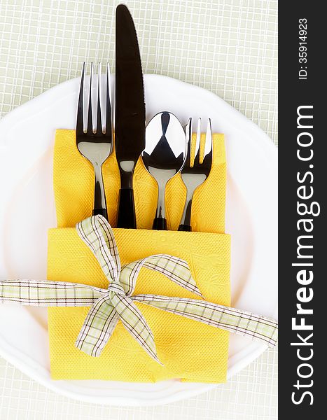 Elegant Table Setting with Fork, Table Knife, Spoon and Dessert Fork into Yellow Napkin Decorated with Green Checkered Bow on White Plate