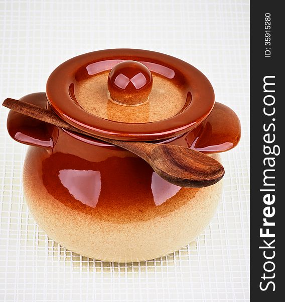 Brownish Stoneware Pot and Wooden Spoon under Lid isolated on Light Green Checkered background. Brownish Stoneware Pot and Wooden Spoon under Lid isolated on Light Green Checkered background