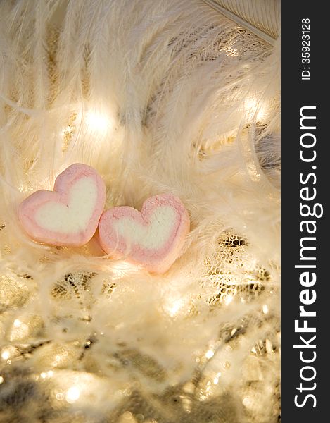Two heart marshmallow on soft feathers and lights