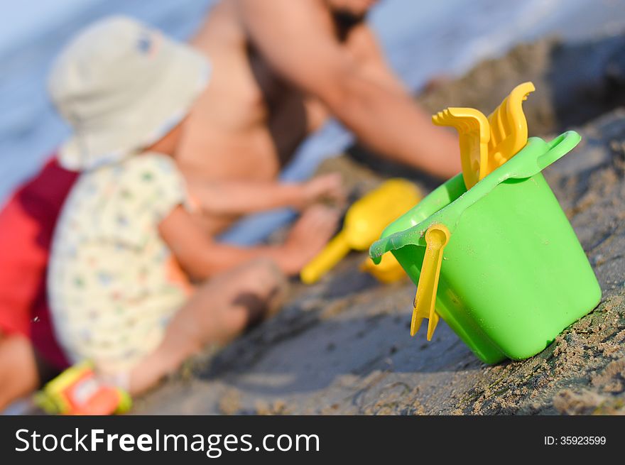 Father and son playng on sandy beach toys closer to viewer. Father and son playng on sandy beach toys closer to viewer
