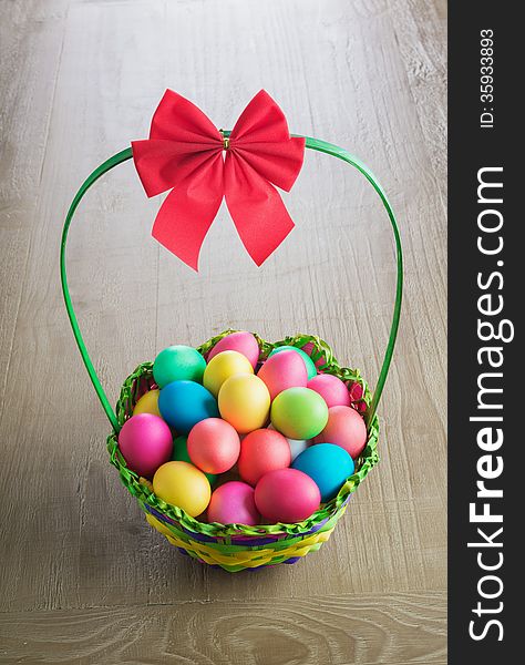 Multicolored Easter eggs in the wattled basket on vintage wooden table