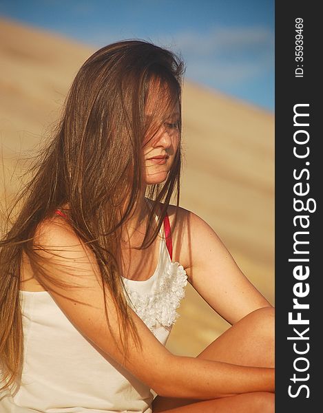 A shy or depressed looking teenager allows a summer sea breeze to blow her long hair around her face . A shy or depressed looking teenager allows a summer sea breeze to blow her long hair around her face .