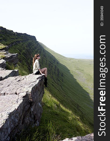 Beautiful young girl sitting on the top of the high cliff in mountains. Beautiful young girl sitting on the top of the high cliff in mountains