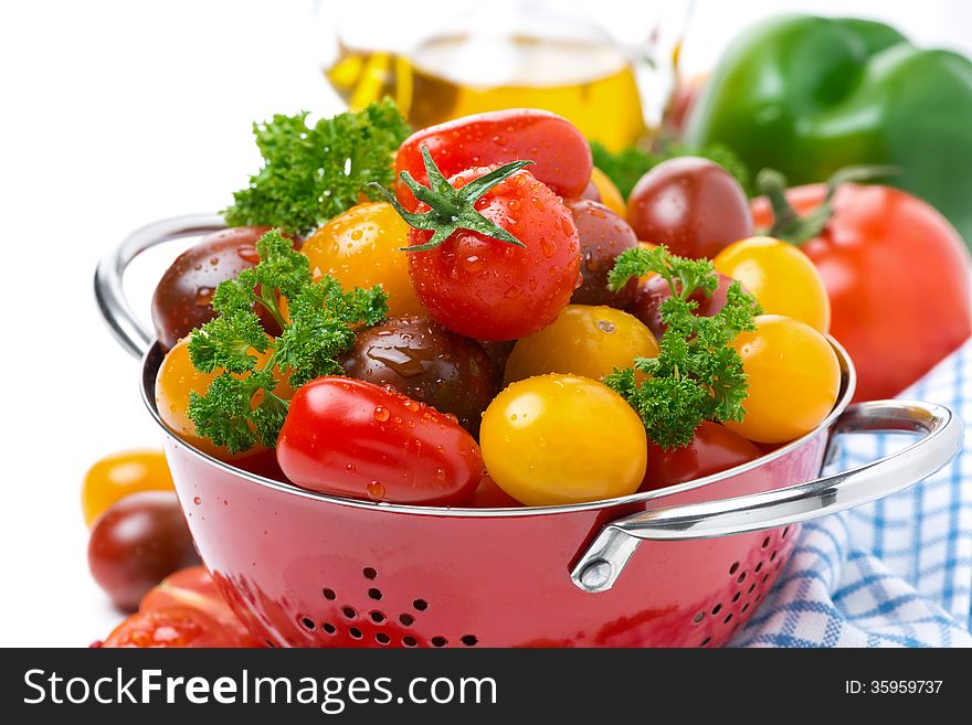 Assorted cherry tomatoes and greens in a colander, close-up, horizontal