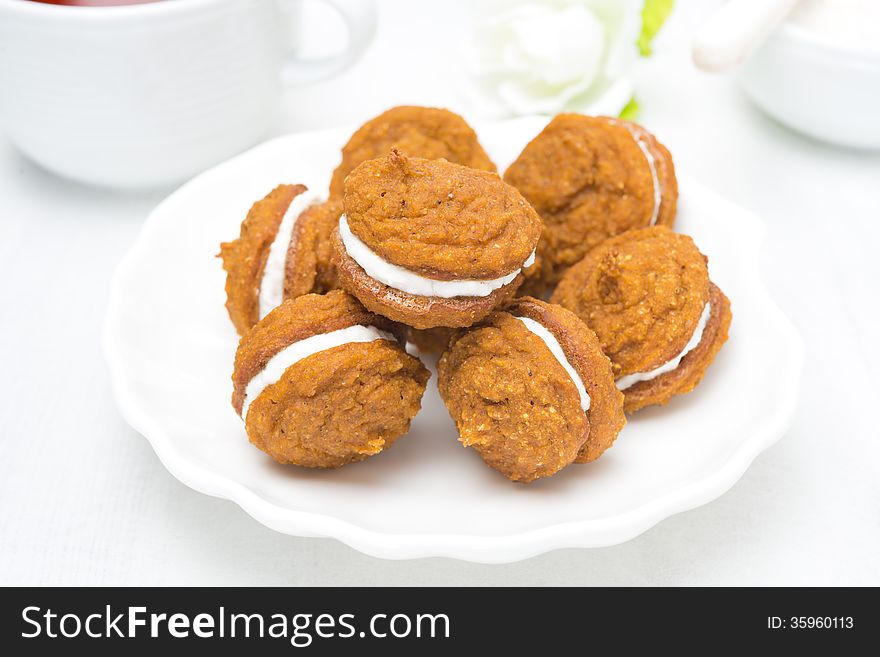 Pumpkin cookies with cream filling on a white plate, close-up