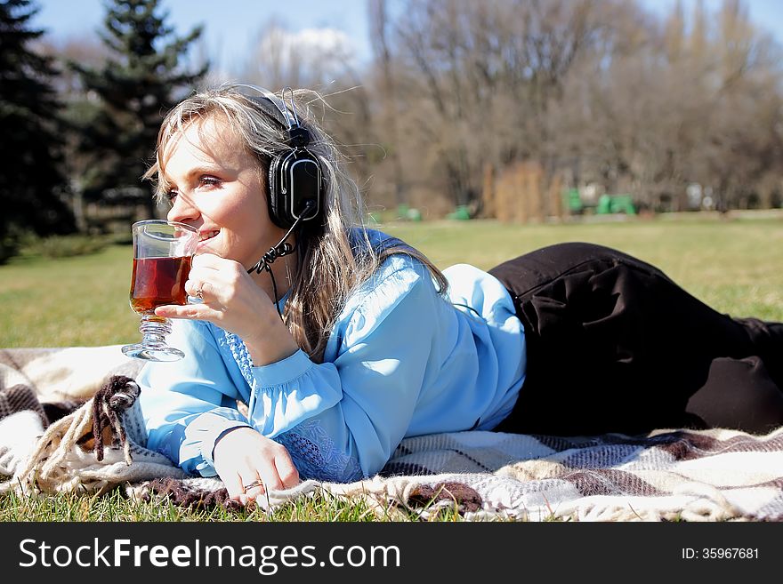 Girl on a picnic, holding a cup of tea in hand and listens to music through headphones. Girl on a picnic, holding a cup of tea in hand and listens to music through headphones